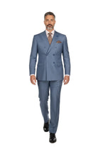 A man wearing a blue double-breasted suit with a patterned tie and pocket square, walking forward against a plain white studio background.