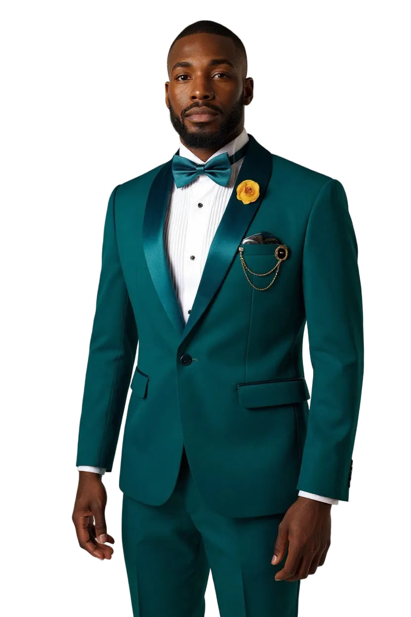 A man wearing a teal emerald green tuxedo with satin peak lapels, a white pinstripe shirt, a matching teal bow tie, and a yellow flower boutonniere, standing against a light gray studio background.