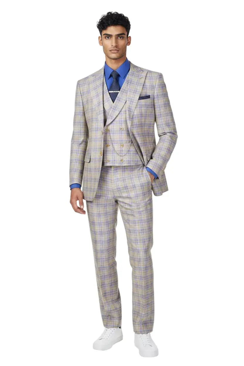A man modeling a light beige and blue plaid three-piece suit with a blue shirt, blue tie, and white sneakers against a white studio background.
