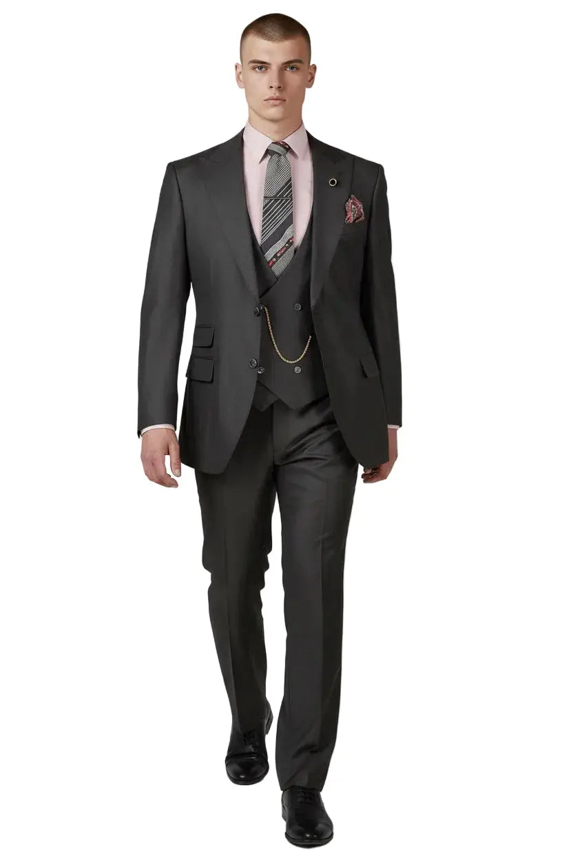 A man modeling a dark charcoal gray three-piece suit with a light pink dress shirt, a patterned gray tie, and a pocket square, standing against a light gray studio background.