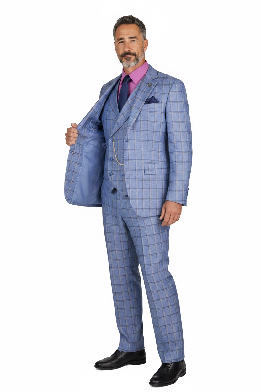 A man modeling a light blue three-piece suit with a subtle windowpane plaid pattern, styled with a pink shirt, purple tie, and black dress shoes against a plain white background.
