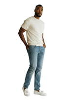 A man modeling a cream short-sleeve crewneck t-shirt, light blue slim-fit jeans, and white slip-on sneakers against a plain white studio background.