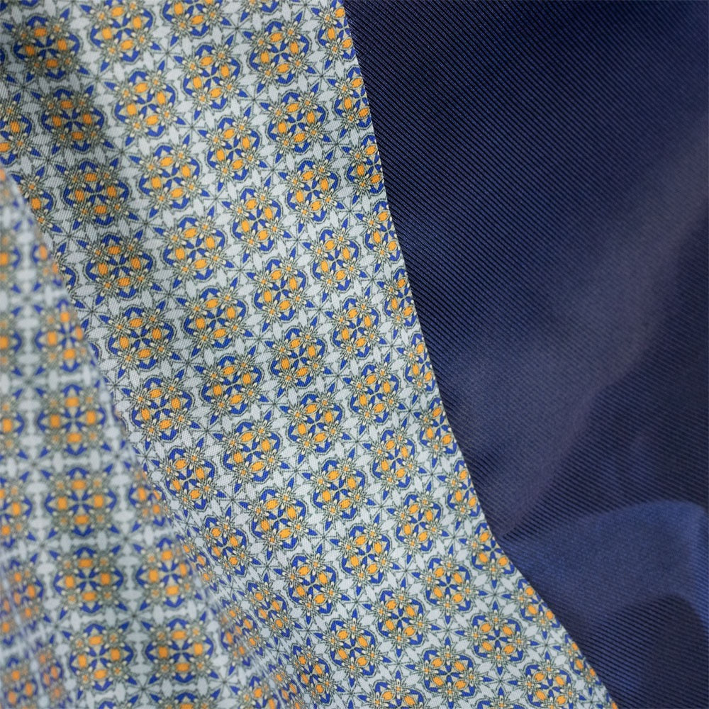 Close-up of a patterned fabric with a repeating geometric medallion design in blue, gold, and white, layered over a solid dark navy blue fabric.