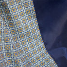Close-up of a patterned fabric with a repeating geometric medallion design in blue, gold, and white, layered over a solid dark navy blue fabric.
