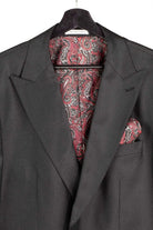 A dark charcoal gray suit jacket displayed on a black hanger, featuring a matching red, black, and white paisley patterned dress shirt and pocket square in the breast pocket.