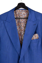A royal blue suit jacket displayed on a black hanger, featuring a matching paisley patterned pocket square and matching patterned dress shirt visible inside the collar.