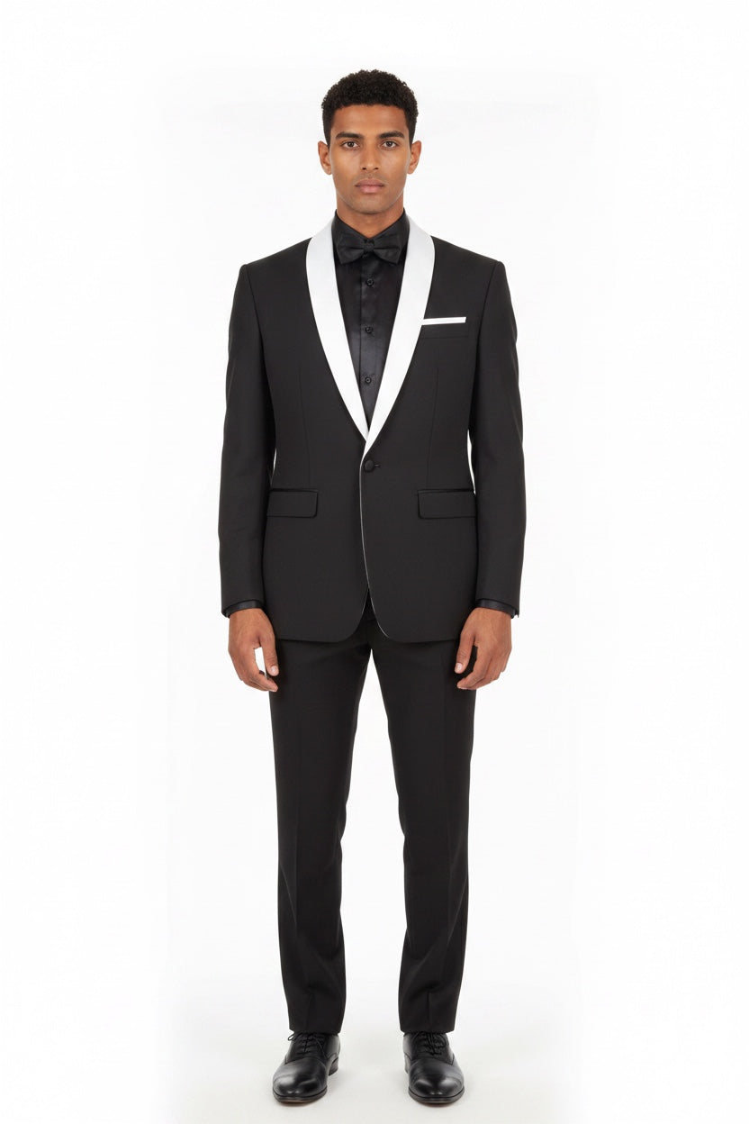 A man modeling a black tuxedo with white satin lapels, a black shirt, a black bow tie, and a white pocket square, shot against a plain white studio background.