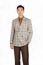 A man modeling a beige and brown plaid double-breasted blazer, paired with a green shirt, rust-colored tie, and brown trousers, against a plain white background.