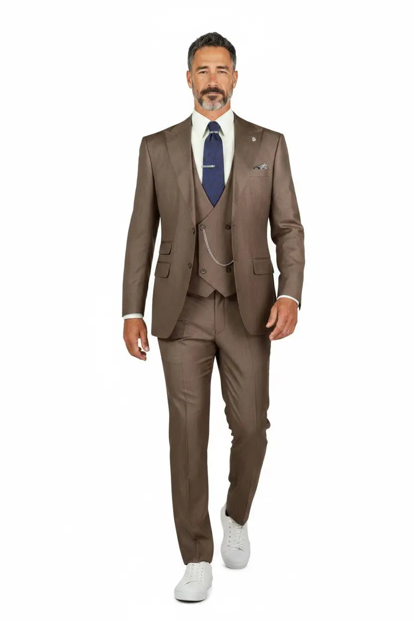 A man modeling a three-piece brown suit with a white dress shirt, a blue patterned tie, and white sneakers against a plain white background.