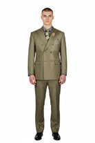 A man modeling a double-breasted olive green suit with a patterned shirt, tie, and pocket square, standing against a solid white background.