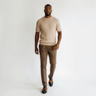 A man modeling a light beige short-sleeve knit sweater and brown trousers against a plain white studio background.