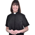 A woman wearing a black M & R Clothing short sleeve clergy shirt with a white tab collar against a white background.