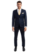 A man wearing a M & R Clothing navy blue skinny-fit 3-piece suit with a white shirt, yellow tie, and black shoes.